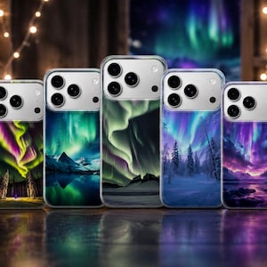Op de afbeelding: Vijf doorzichtige telefoonhoesjes op een rij, elk met een uniek geprint ontwerp van het noorderlicht boven besneeuwde landschappen, bergen en bossen. De hoesjes hebben een uitsparing voor de camera aan de bovenkant en een glanzende afwerking.