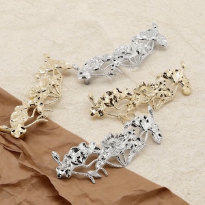 May include: A selection of decorative floral cabinet pulls in gold and silver. The metal pulls feature a detailed flower and leaf design. The pulls are arranged on a brown surface.