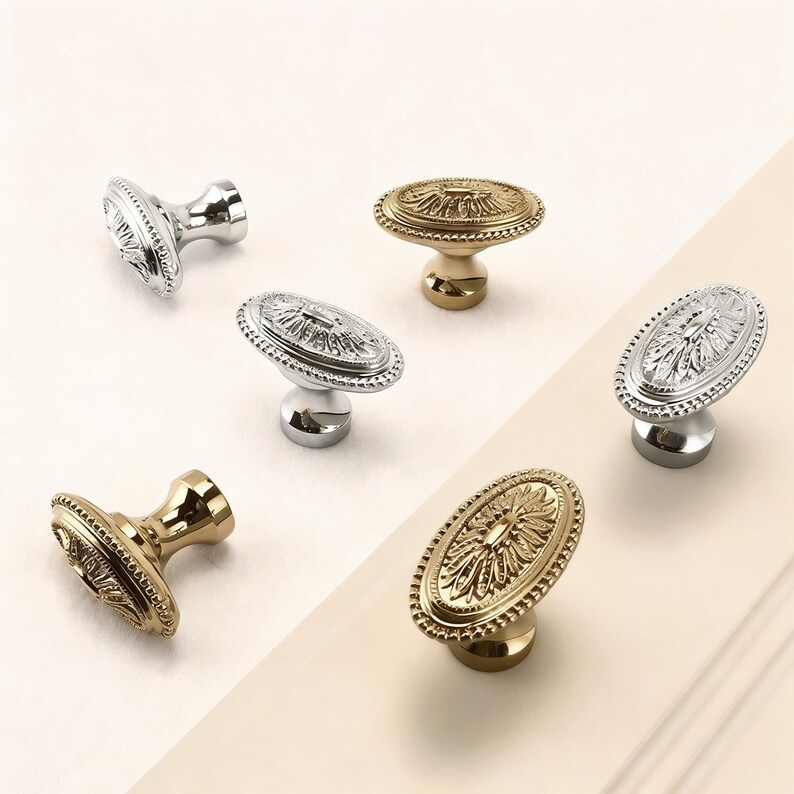 May include: An assortment of decorative cabinet knobs in gold and silver finishes. The knobs have an oval shape with ornate floral detailing and a raised base. The hardware is designed for furniture and home decor.