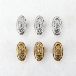 May include: Six oval cabinet knobs in two finishes: silver and gold. Each knob features a detailed floral design within an oval frame with a beaded edge. The knobs are arranged in two rows of three against a white background.