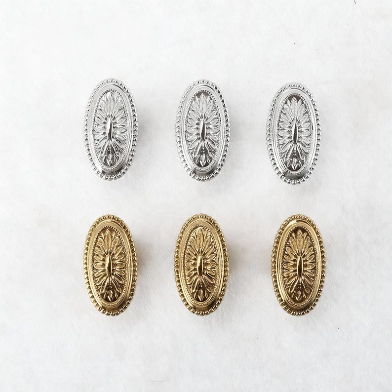 May include: Six oval cabinet knobs in two finishes: silver and gold. Each knob features a detailed floral design within an oval frame with a beaded edge. The knobs are arranged in two rows of three against a white background.
