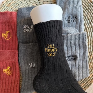 May include: Selection of socks in red, grey, and black, with embroidered text. The black sock features "T&L Happy 3nd!" in gold. Other socks display "Mr & Mrs", dates, and phrases such as "Forever to go" and "Years down".