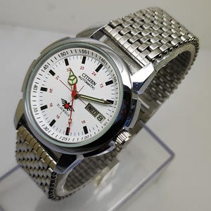 May include: A silver-toned Citizen automatic wristwatch with a white face. The watch features a silver band, red and green hands, and the day of the week displayed. The watch face includes the text "CITIZEN AUTOMATIC" and "21 JEWELS".