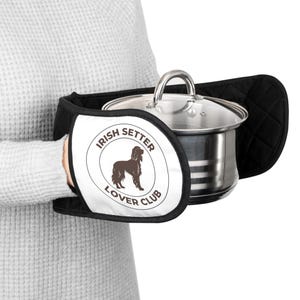 May include: Black and white Irish Setter Lover Club oven mitts holding a stainless steel pot with a glass lid. The mitts have a quilted design and a circular logo with an Irish Setter silhouette.