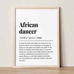 May include: A framed print with the words "African dancer" in bold black font. Below, the phonetic pronunciation and a definition describe a rhythmic warrior. The print is in a light wood frame.