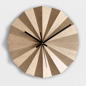 May include: A modern wall clock with a geometric design. The clock face is divided into alternating shades of beige and brown, radiating from the center. Black clock hands indicate the time. The clock's diameter is approximately 12 inches.