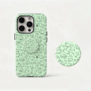 May include: A mint green phone case and matching pop socket featuring a repeating pattern of black line-drawn cats in various poses. The phone case has a camera cutout and black side buttons.