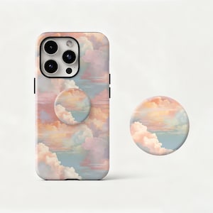 Peut inclure: Une coque de téléphone et un PopSocket assorti avec un motif de nuages pastel dans les tons rose, pêche et bleu. La coque a un bord noir et une découpe pour l'appareil photo. Le PopSocket est rond et présente le même motif de nuages.