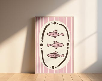 May include: A framed art print featuring three pink fish illustrations within a dark brown oval frame. The background is a light pink with vertical white stripes. The artwork is displayed on a wooden floor against a beige wall.