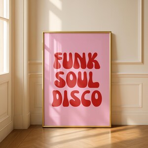 May include: A framed pink poster with the words "FUNK SOUL DISCO" in red, retro-style lettering. The poster is in a gold frame and leans against a wall. The room has a wooden floor and a door.