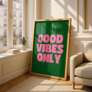 Könnte beinhalten: Ein gerahmtes Poster mit grünem Hintergrund und den Worten "GOOD VIBES ONLY" in großen, rosa Buchstaben. Das Poster hat einen Naturholzrahmen und lehnt an einer Wand. Der Raum hat ein Fenster und einen beigen Sessel.