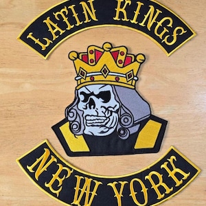 May include: Embroidered patches with the text "LATIN KINGS" and "NEW YORK". The central patch features a skull wearing a crown. The patches are black with yellow and gold accents.
