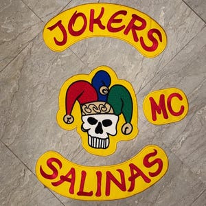 May include: Embroidered patches with the words "JOKERS" and "SALINAS" in red, arched over and under a central patch with a skull wearing a jester's hat. The letters "MC" are also included. All patches have a yellow background.