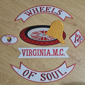 May include: Embroidered patches with motorcycle club themes. Includes a wheel design with a yellow wing, banners with "WHEELS" and "OF SOUL", and a diamond-shaped patch with "1%ER" text. The patches are red, white, and black.