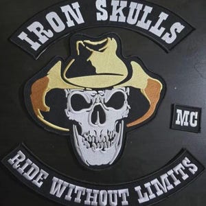 Może przedstawiać: Haftowana naszywka z napisem "IRON SKULLS" nad czaszką w kapeluszu kowbojskim. Naszywka zawiera również napisy "RIDE WITHOUT LIMITS" i "MC". Projekt wykorzystuje kolory biały, czarny i brązowy.