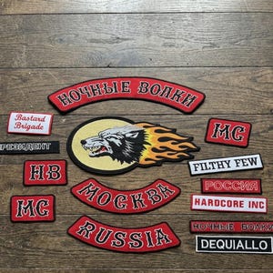 May include: A collection of embroidered patches featuring a central wolf head with flames, arched rockers with the text "НОЧНЫЕ ВОЛКИ", "МОСКВА", and "RUSSIA", and rectangular patches with text including "Bastard Brigade", "MG", "FILTHY FEW", "ПРЕЗИДЕНТ", "РОССИЯ", "HARDCORE INC", and "DEQUIALLO".