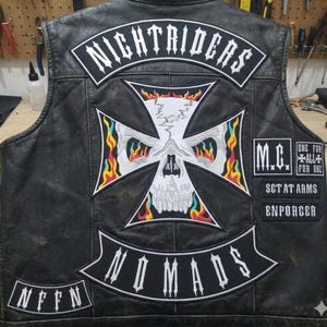 May include: Black leather vest with patches. The back features a large skull and crossbones design with flames, the word "NIGHTRIDERS" across the top, and "NOMADS" below. Additional patches include "M.C.", "SET AT ARMS", and "ENFORCER".