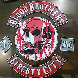 Puede incluir: Un conjunto de parches bordados con temática motera. El parche principal presenta una calavera roja y negra con las palabras "BLOOD BROTHERS" y "LIBERTY CITY". Parches adicionales incluyen "1%" y "MC".