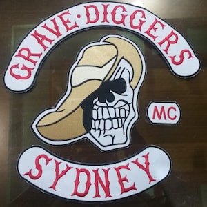 Puede incluir: Conjunto de parches bordados con una calavera con sombrero de vaquero. El conjunto incluye las palabras "GRAVE DIGGERS" en un diseño curvo, "SYDNEY" en un diseño curvo y "MC" en un pequeño rectángulo. Los parches tienen fondo blanco con detalles rojos y dorados.