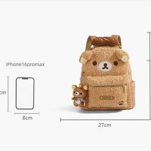 May include: A brown teddy bear-shaped backpack with a small bear plushie attached. The backpack is 31cm tall, 27cm wide, and 14cm deep. It has a front pocket and adjustable straps. The top handle is 6cm. The image also shows an iPhone 16 promax.