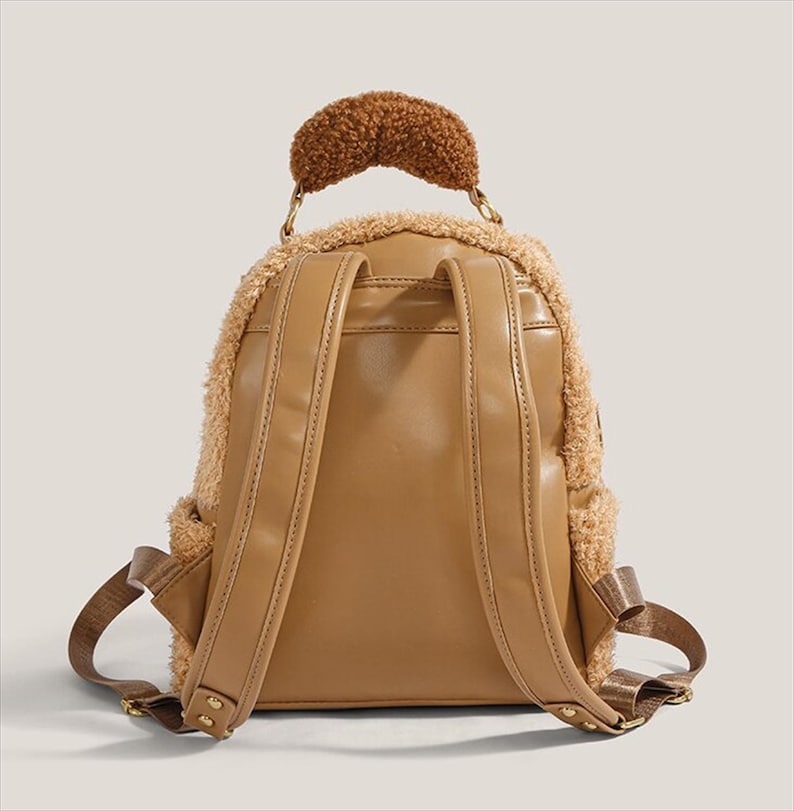 May include: A tan backpack with a fluffy, teddy bear-like texture around the edges and a brown, textured handle. The back of the backpack is smooth tan leather with adjustable straps and a small pocket.