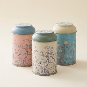 Tea coffee sugar canister set for kitchen counter storage, featuring three vintage botanical floral kitchen canisters in pastel pink, cream, and teal colors with decorative ceramic lids, isolated on a clean neutral studio background for farmhouse cottagecore home organization.