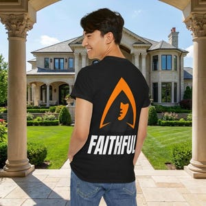 Puede incluir: Camiseta negra con un diseño gráfico naranja y la palabra "FAITHFUL" en blanco. El gráfico es una forma estilizada con una silueta de rostro. La persona lleva vaqueros azules.