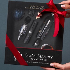 May include: A black rectangular gift box containing a wine accessory set labeled SipArt Mastery Wine Wizard Trio. The set includes a wine aerator, a cylindrical opener, and a stopper. The box features white text and a red ribbon tied around the exterior.