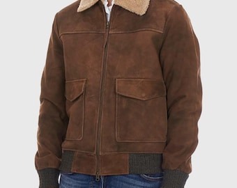 May include: A brown suede bomber jacket with a tan shearling collar. The jacket has two front pockets, a ribbed hem, and cuffs. The jacket is zipped up and has a classic, vintage style.
