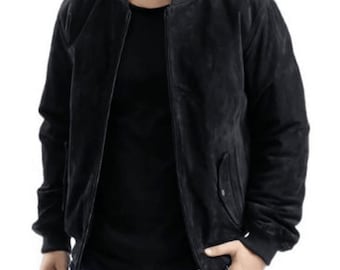 May include: A black suede bomber jacket featuring a ribbed collar, cuffs, and hem. The jacket has a full-length front zip closure and two side pockets with snap button details. It is worn over a plain black t-shirt and dark blue denim jeans.