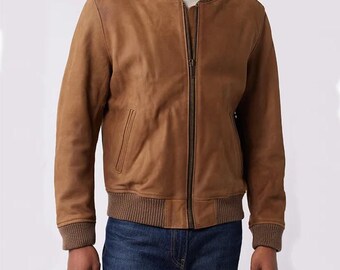 May include: A brown leather bomber jacket with a ribbed collar, cuffs, and hem. The jacket features a zip-up front and two side pockets. The model is wearing blue jeans. A classic outerwear piece.