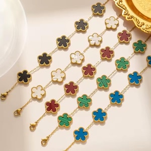 May include: Five gold-tone link bracelets, each featuring a series of flower-shaped charms. The charms are inlaid with various colours including black, white, maroon, green, and blue. Each bracelet is finished with a lobster claw clasp.