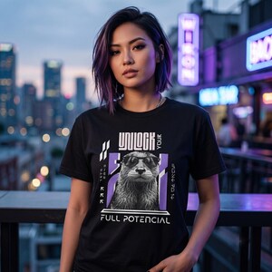 May include: Black t-shirt with a graphic of an otter wearing sunglasses and the words "UNLOCK YOUR FULL POTENCIAL". The design includes purple and white accents. The shirt is worn by a person with purple-streaked hair.