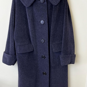 May include: A dark purple wool-textured coat featuring a wide rounded collar, long sleeves with folded cuffs, and a front button closure with five matching dark circular buttons. The coat includes two side pockets with flaps and a smooth lining.