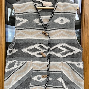 May include: A sleeveless vest with a geometric pattern in shades of gray, beige, and white. The vest has two front pockets and wooden toggle closures. The brand name "DOROTHY PERKINS" is visible on the label.