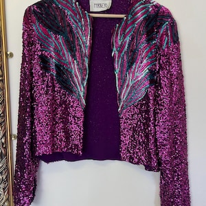 May include: A vintage, open-front jacket covered in shimmering magenta sequins. Teal and fuchsia feather-like designs adorn the front. The jacket has long sleeves and a deep purple lining. The label reads "PARKERS".