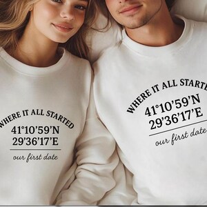 May include: Two people wearing white sweatshirts with the text "WHERE IT ALL STARTED" and coordinates 41°10'59"N 29°36'17"E, and "our first date". The sweatshirts are a simple, casual style.