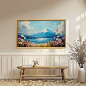 以下が含まれることがあります： 額入りの風景画は、雪をかぶった山、湖、色とりどりの野花を描いています。このアートワークは、雲のある青い空と金色のフレームが特徴です。絵は木製のベンチの上に飾られています。