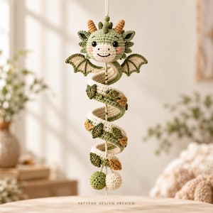 May include: A hanging crochet dragon ornament featuring a coiled body in shades of sage green and cream. The dragon has small wings, tan horns, and is decorated with small crocheted leaves along its spiral length, ending in two round spheres.