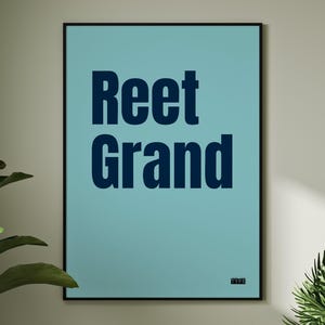 Puede incluir: Un póster enmarcado con las palabras "Reet Grand" en letras de bloque azul oscuro sobre un fondo azul claro. El póster tiene un marco negro y un pequeño texto en la esquina inferior derecha. Una planta verde es visible a la izquierda.