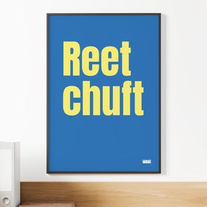 Puede incluir: Una impresión artística enmarcada con un fondo azul y el texto amarillo "Reet Chuft". La obra de arte se exhibe en una pared blanca sobre un escritorio de madera. Se ven una pequeña planta y artículos de oficina.