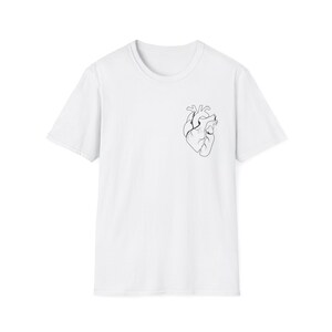 Puede incluir: Camiseta blanca con un contorno negro minimalista de un corazón humano en el pecho izquierdo. La camiseta tiene cuello redondo y mangas cortas. El diseño es simple y gráfico.