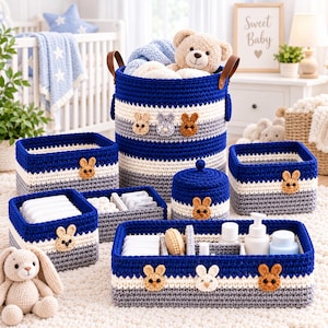 May include: A set of crocheted storage baskets in blue, white, and grey, featuring small bunny face appliques. The set includes a tall round hamper with leather handles, several rectangular bins, and a lidded jar, all containing baby items.