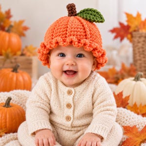 May include: A bright orange crocheted pumpkin hat with a brown stem and a green leaf, featuring a ruffled brim. The hat is worn with a long-sleeved, cream-colored knit onesie that has three small, round, light brown buttons down the front center.