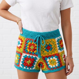 May include: Crochet shorts featuring a vibrant granny square pattern in shades of red, yellow, green, white, and blue. The shorts have a solid teal blue waistband with a matching drawstring tie, constructed from yarn in a multi-colored design.