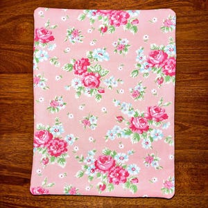 May include: A rectangular, pink floral pattern fabric with a repeating design of large pink roses, small blue flowers, and green leaves. The fabric is likely used for home decor or crafting projects.