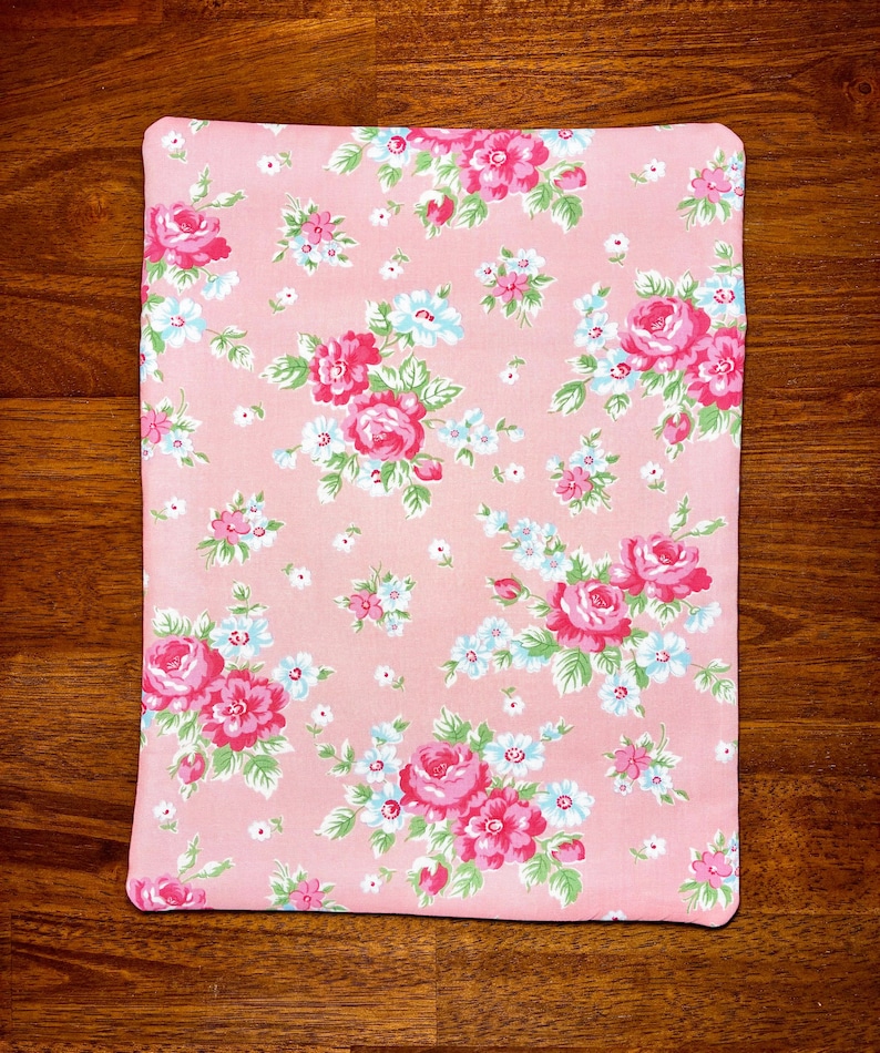 May include: A rectangular, pink floral pattern fabric with a repeating design of large pink roses, small blue flowers, and green leaves. The fabric is likely used for home decor or crafting projects.