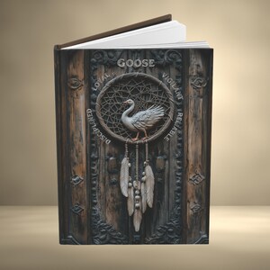 May include: A hardcover book with a dark wood-textured cover featuring a central dreamcatcher design with a white goose at its center. The text GOOSE, LOYAL, VIGILANT, DISCIPLINED, and RELIABLE is printed around the dreamcatcher, which has hanging feathers.