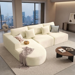 May include: A cream-colored sectional sofa with a textured corduroy-style fabric, featuring a rounded chaise end, multiple back cushions, and several decorative throw pillows in solid cream, brown patterned, and black and white plaid designs.