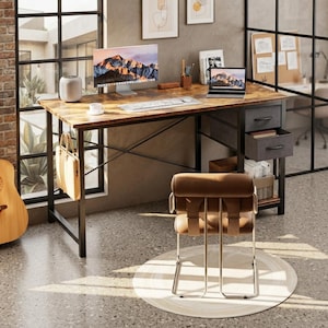 May include: A rectangular computer desk with a rustic brown wood-grain surface and a black metal frame. It features two gray fabric drawers on the right side, a white keyboard, a computer monitor, a laptop, and a tan bag hanging on the side.